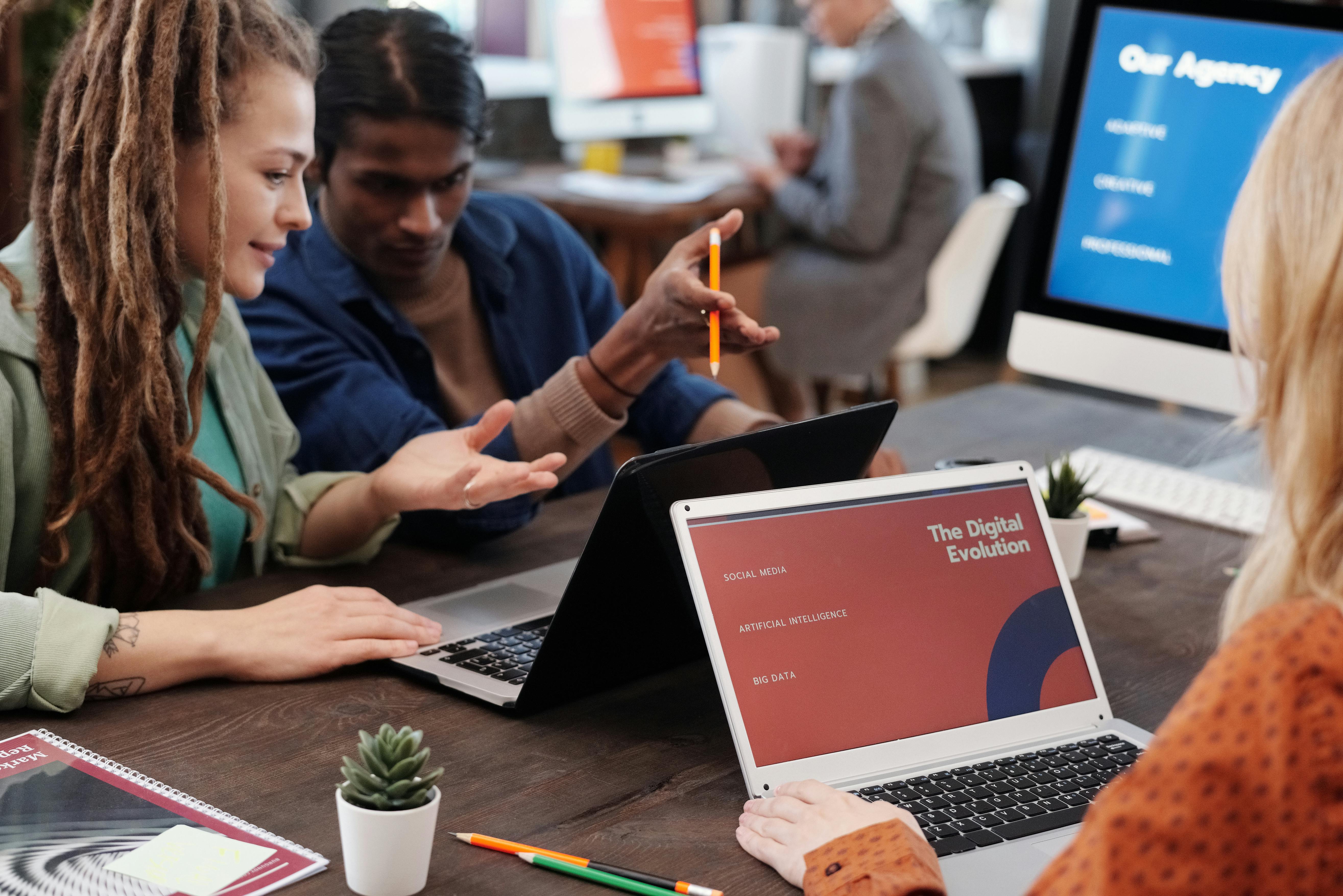 Group of three young diverse professionals collaborating at a desk with a laptop showing "The Digital Evolution."